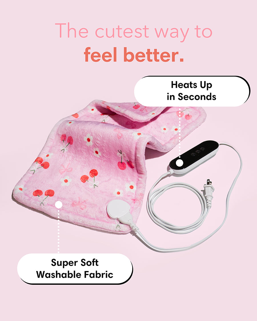 Pink heating pad with cherry pattern and USB cable on a pink background, labeled 'The cutest way to feel better.'